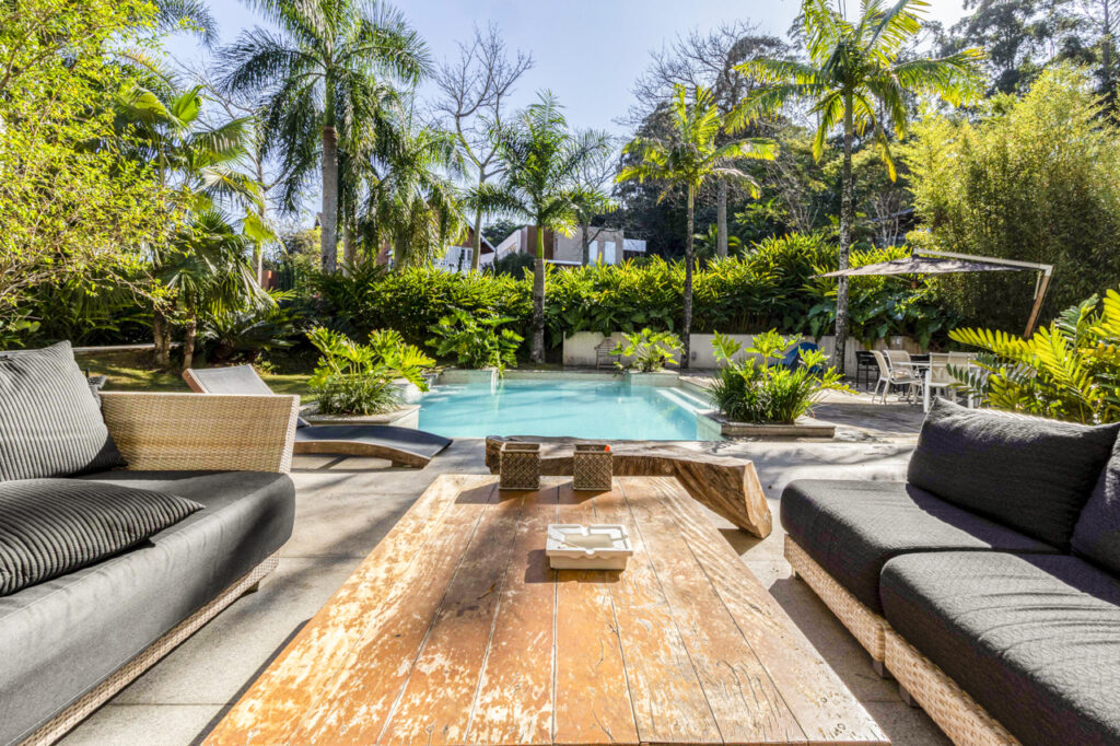 área de convivência em condomínio fechado com piscina cercada por palmeiras e móveis sofisticados
